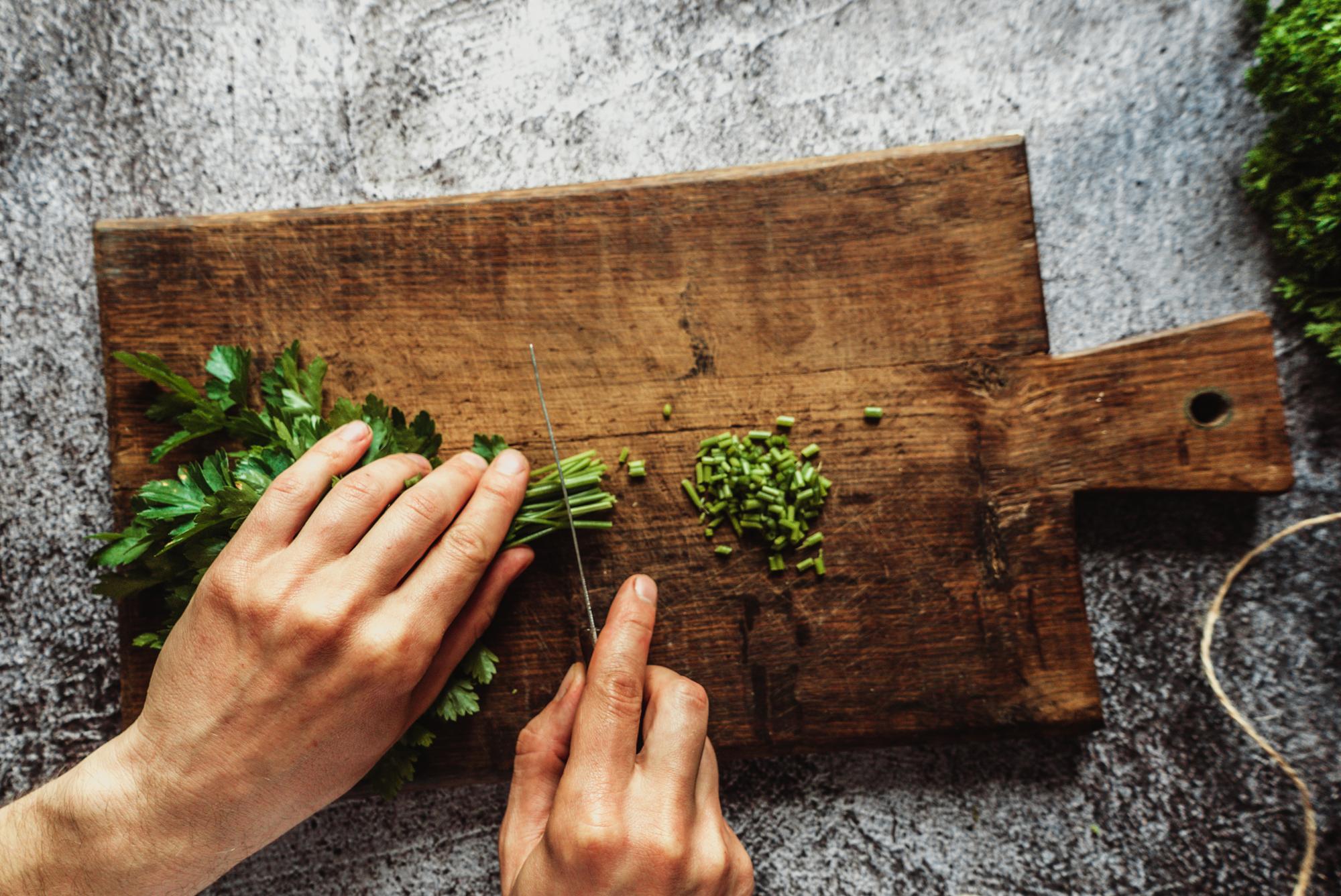 Chef slicing herbs on wooden board